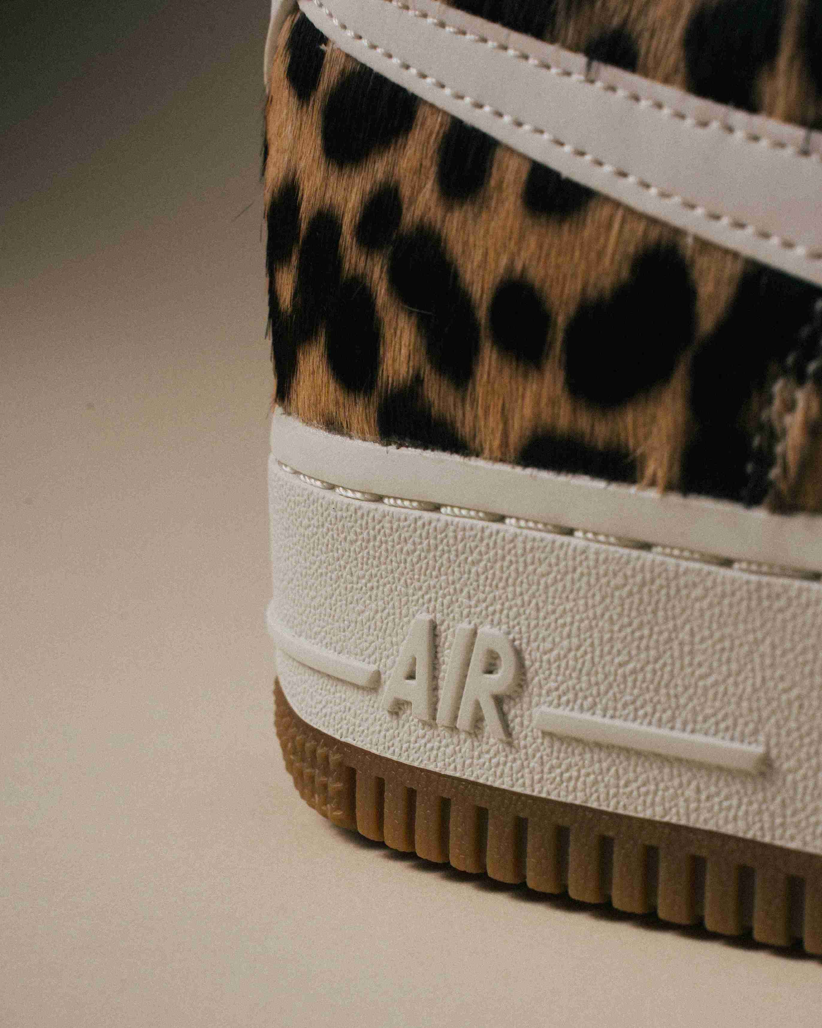 Paire de sneakers Nike Air Force 1 à motif léopard, placée à côté d’une boîte Nike grise sur un fond beige, vue artistique avec lumière douce.